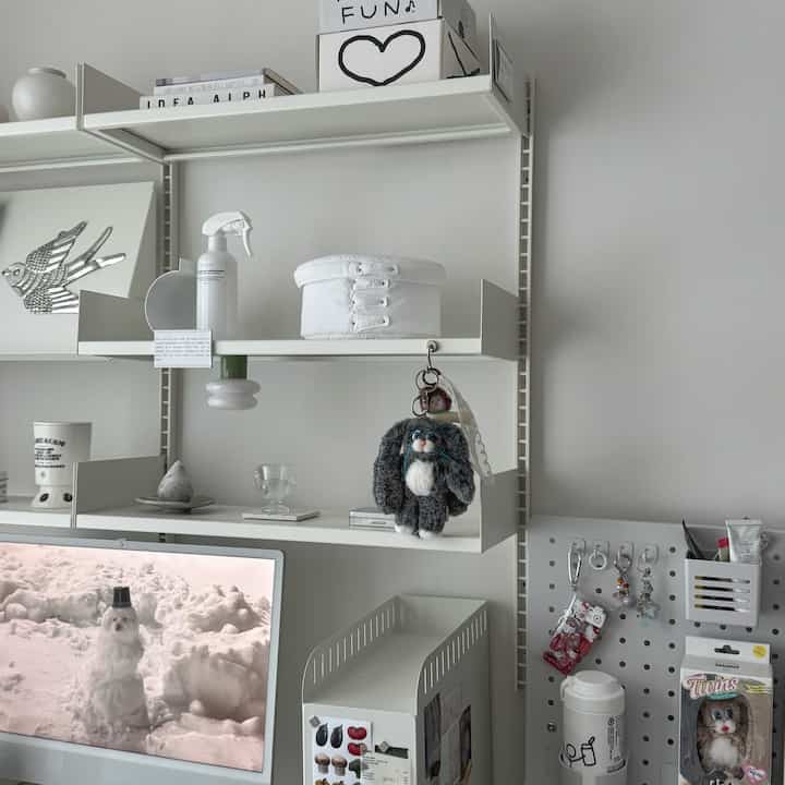 White-toned study space featuring a computer desk, system shelving, and keyring decorations in a clean monotone interior