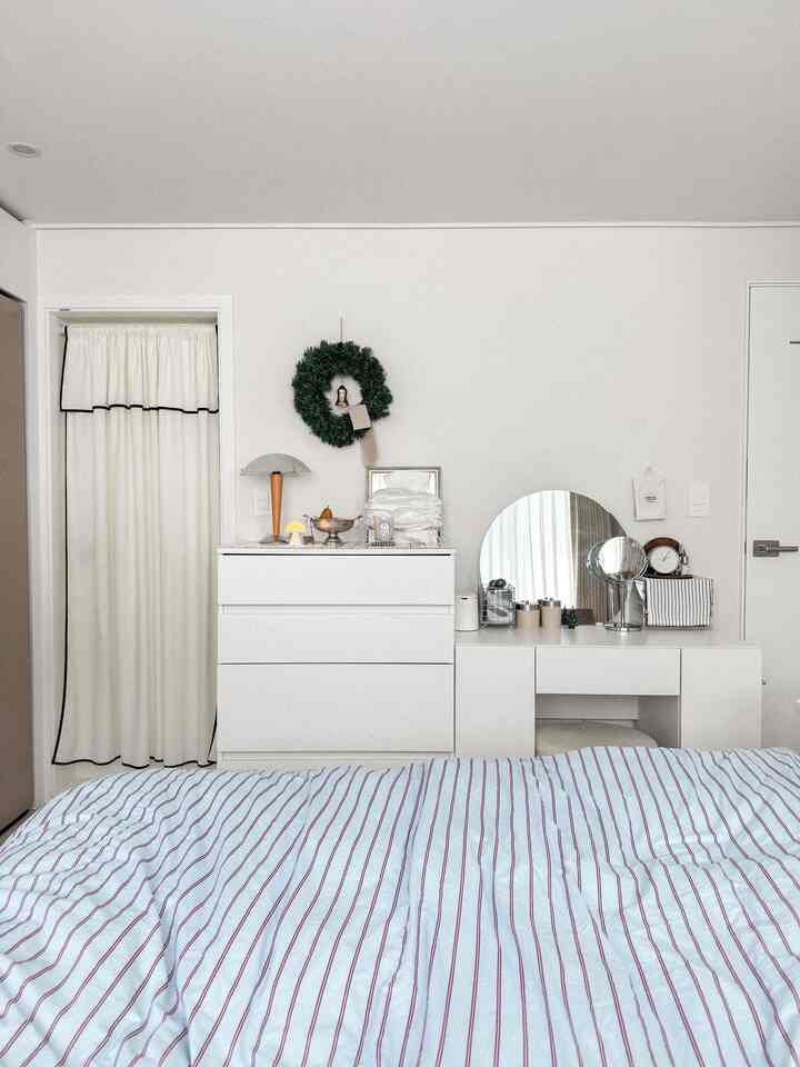 White-toned bedroom featuring a minimal vanity with a round mirror and white dresser, creating a clean and cozy atmosphere