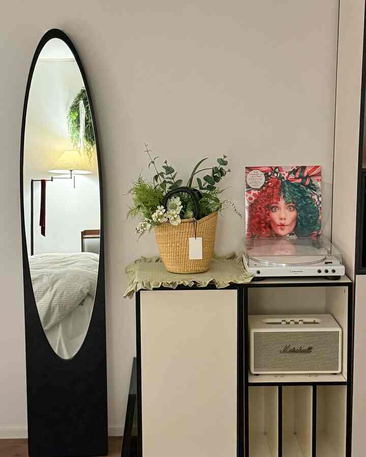白と黒のトーンの寝室、壁際に大きな鏡とフロアランプ、キャビネット上にオーディオテクニカのターンテーブルが配置された雰囲気のあるインテリア