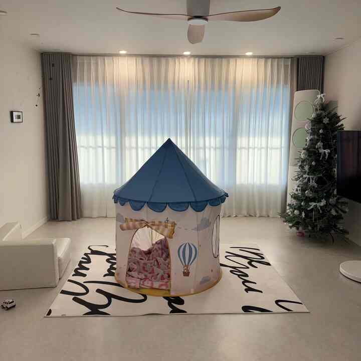 明るいホワイトトーンのモダンなリビング、中央に子供用ブルーテントとクリスマスツリーが配置された空間
