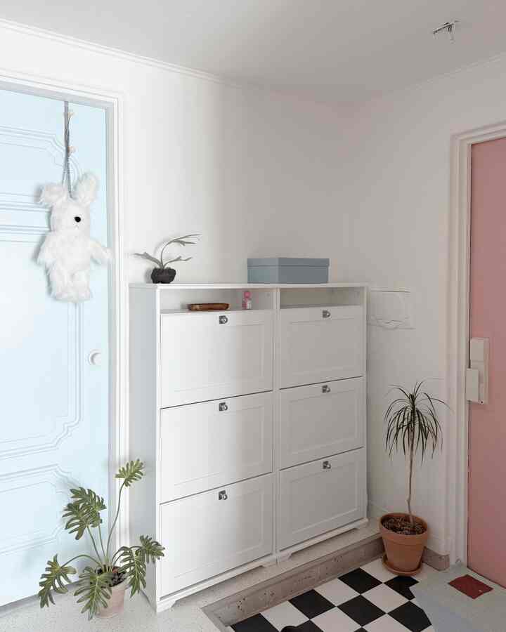 White-toned entrance space featuring a central shoe cabinet, plants, and a pink door creating a neat atmosphere