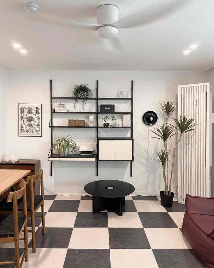 Modern living and dining room featuring white and black tones with wood accents, a round black coffee table centered and wall-mounted shelving
