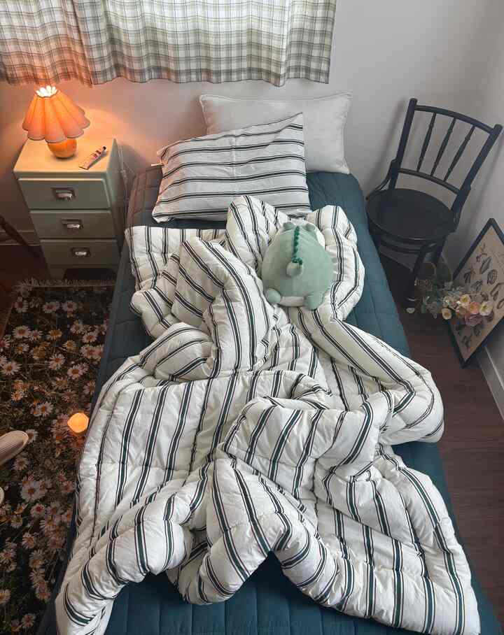 ナチュラルカラーとソフトホワイトの調和が美しい一人用寝室、ストライプ柄の掛け布団カバーとテーブルランプが印象的な雰囲気を演出