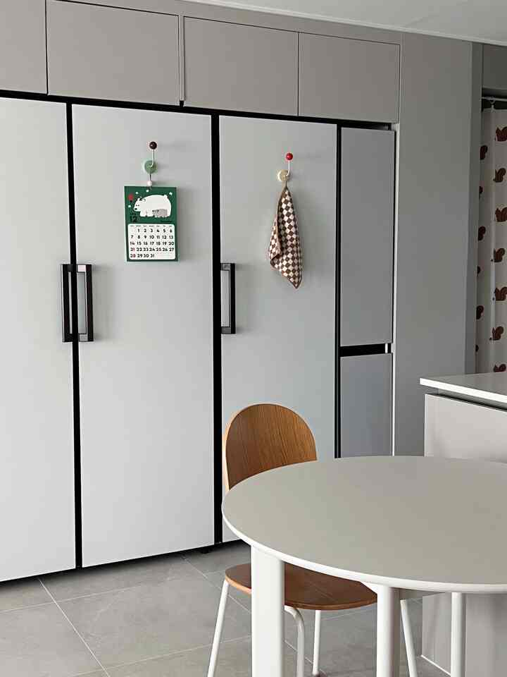 白とグレーのトーンのモダンで清潔感のあるキッチン空間、丸いダイニングテーブルと木目調のチェアが配置されたインテリア