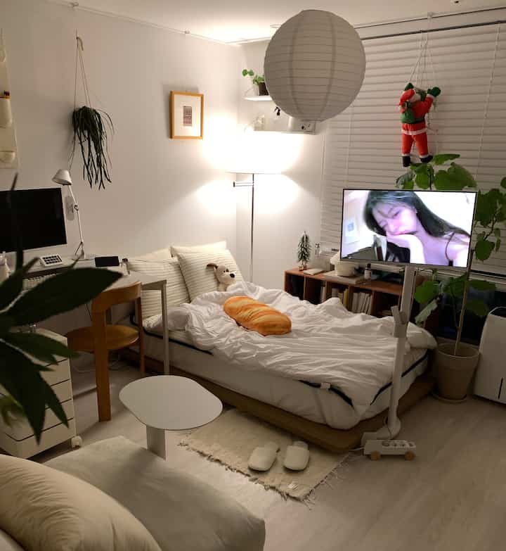 White and wood tone studio apartment room of 6 pyeong featuring low bed frame, sofa, desk, and TV stand with cozy atmosphere