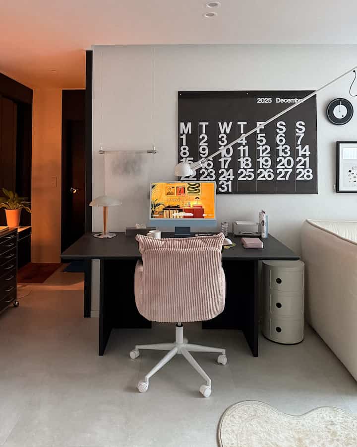 Black and white toned compact living room home office area featuring pink office chair and neat desk setup