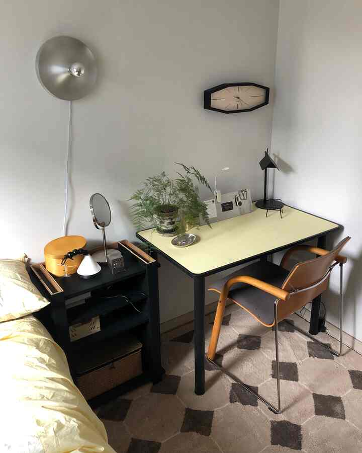 Yellow and black toned bedroom workspace featuring a butter-colored desk, wooden frame chair, wall clock, and potted plant in a vintage mood