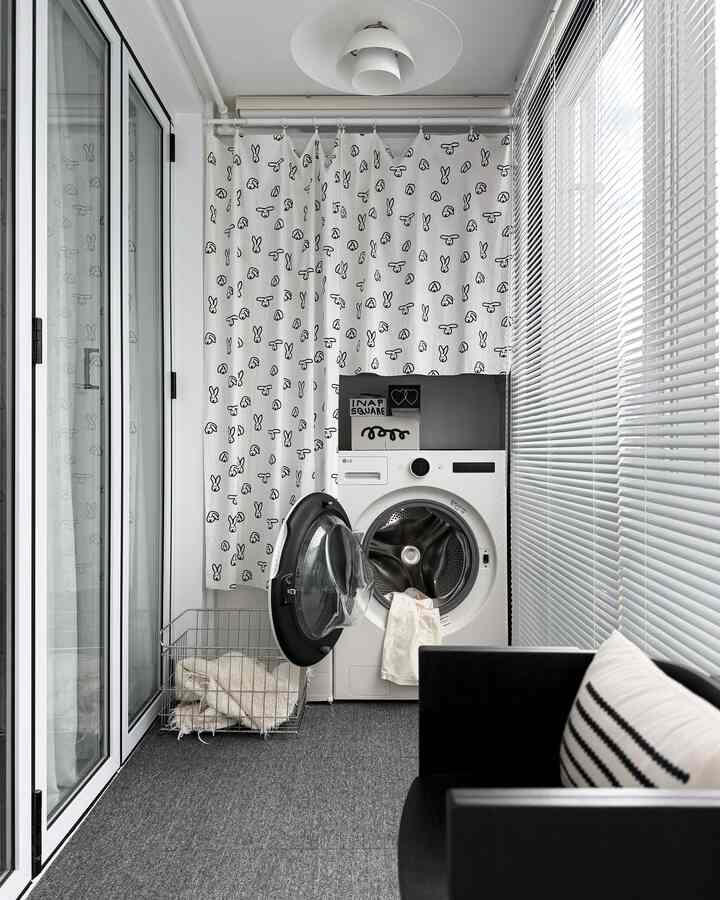 Modern indoor laundry space in a narrow balcony with white and gray tones featuring a washing machine, bunny-pattern curtain, and aluminum blinds