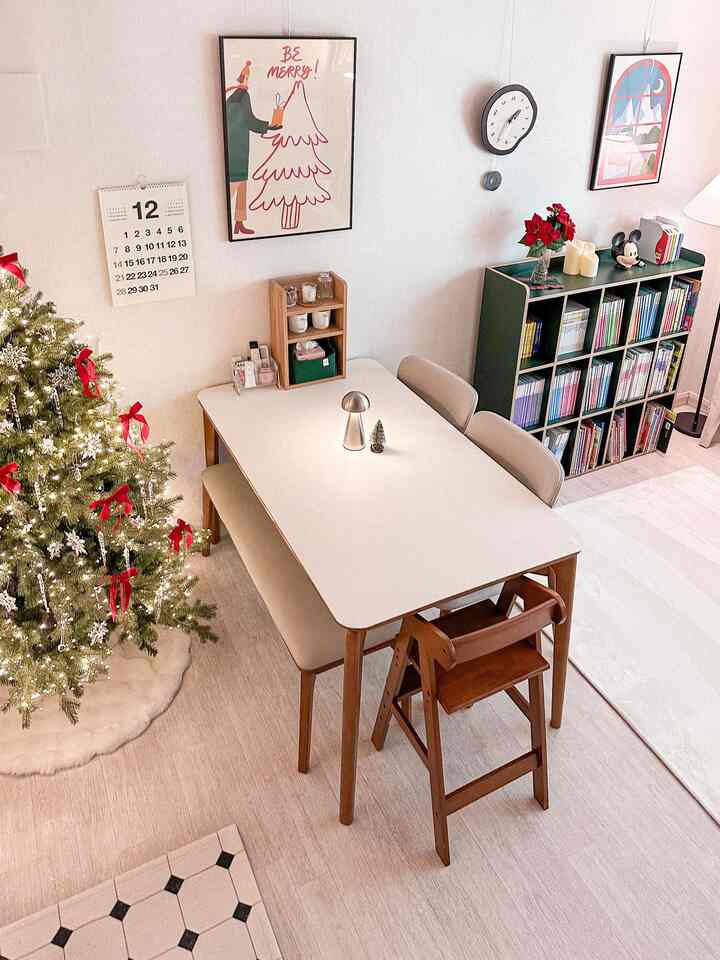 Bright white-walled living room with dining table featuring a silver mood lamp and decorated Christmas tree, creating a warm holiday atmosphere