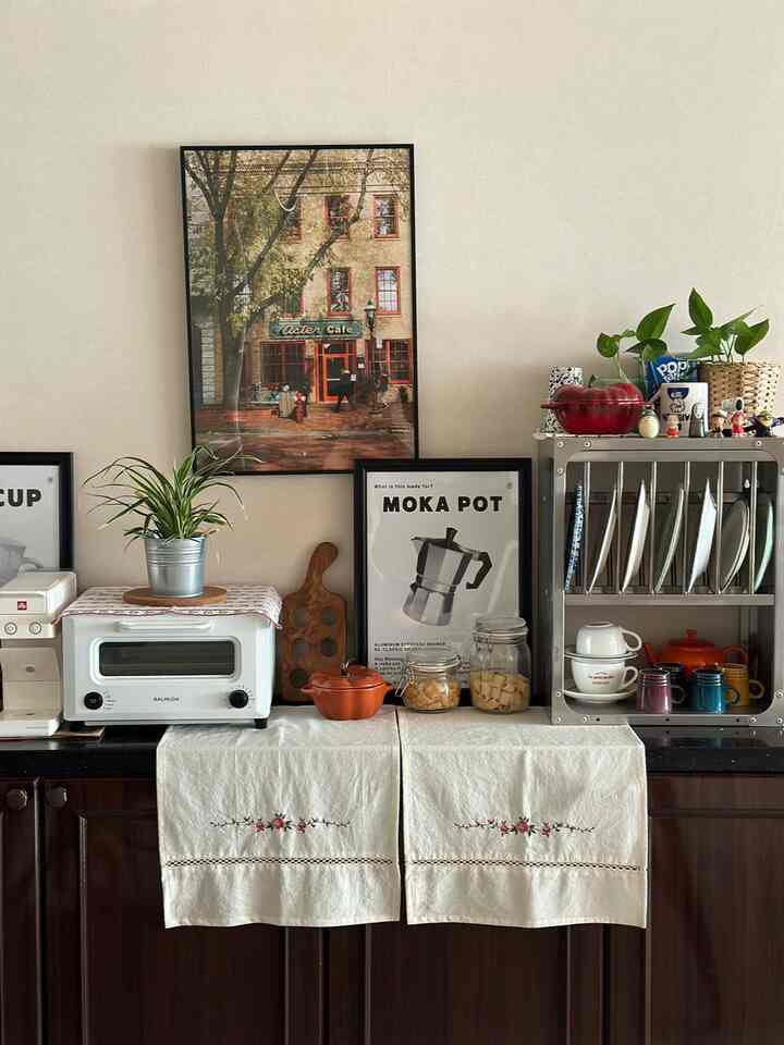 白い壁とキッチン家電、花柄刺繍のヴィンテージ風タオルが配置された居心地の良いおうちカフェのキッチン