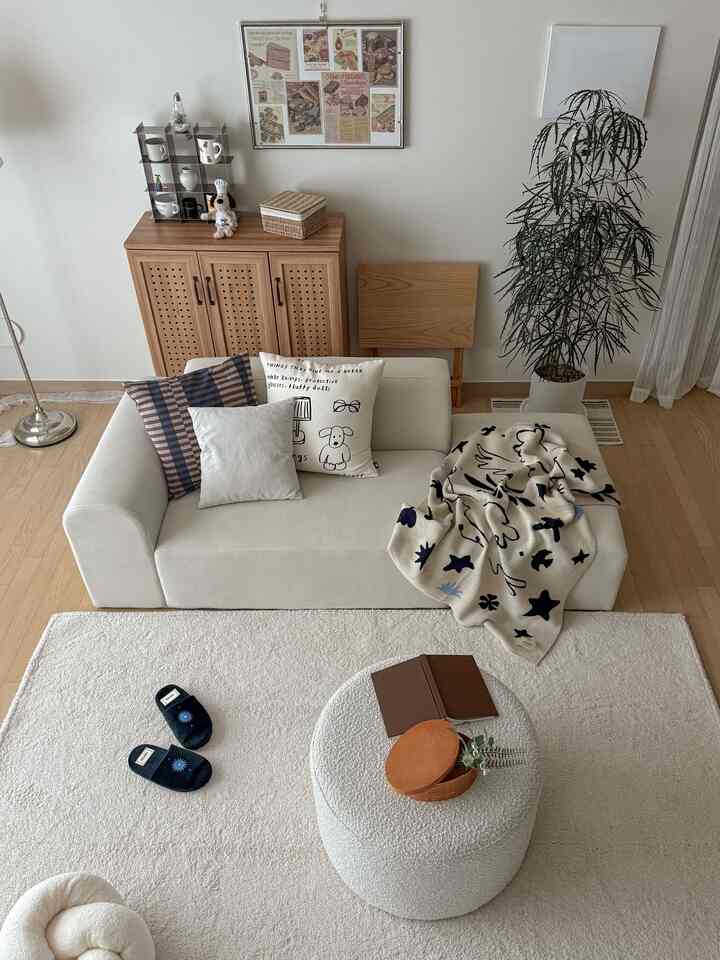 白とベージュの色調のリビング、ソファとスツール、ラグが配置された温かみのあるシンプルな空間