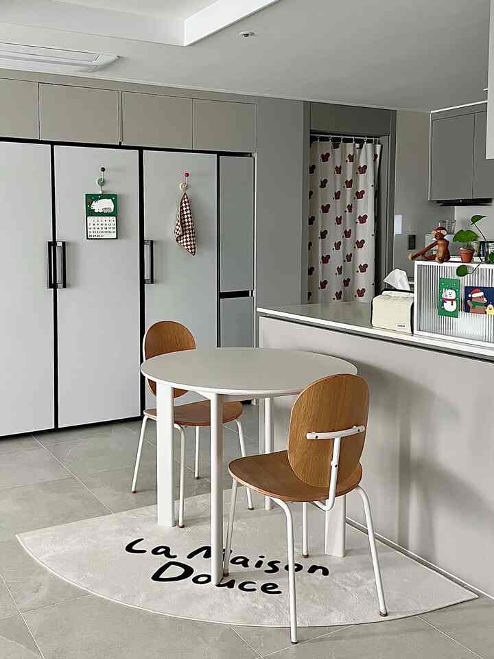 白とグレー調のキッチンスペース、ラウンドダイニングテーブルとナチュラルな木製チェアが配置された落ち着いた二人用ダイニング