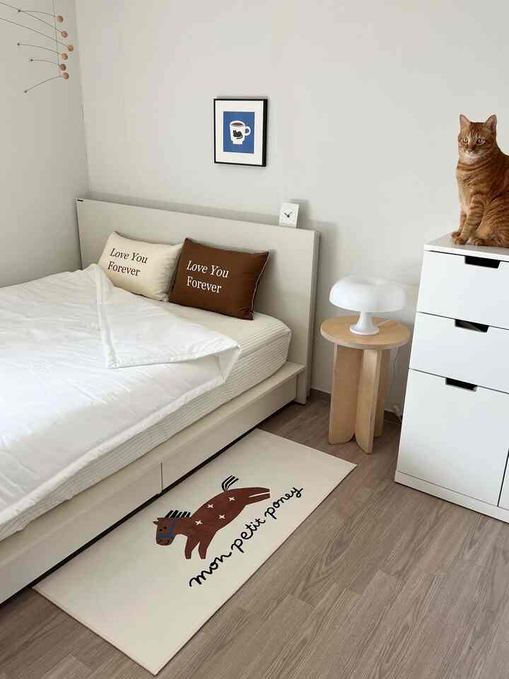 白とナチュラルブラウンのトーンの寝室、愛のメッセージ入りの枕と猫がいる落ち着いた空間