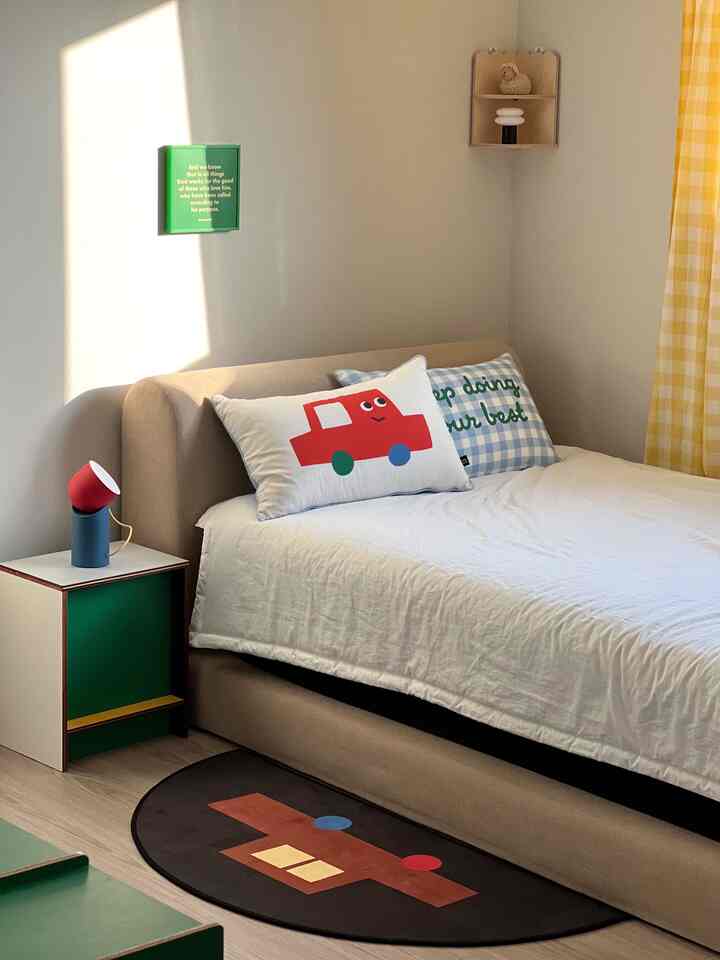 白と黄色のトーンの子供部屋、ベージュのベッドとかわいい車柄のクッションが配置されたシンプルで暖かみのあるインテリア