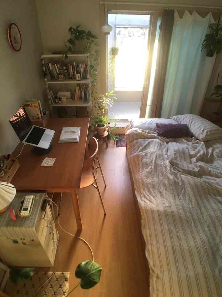 温かみのある木目調と自然光が調和した、小さな一人暮らしの寝室、デスクと植物が配置されたナチュラルな空間