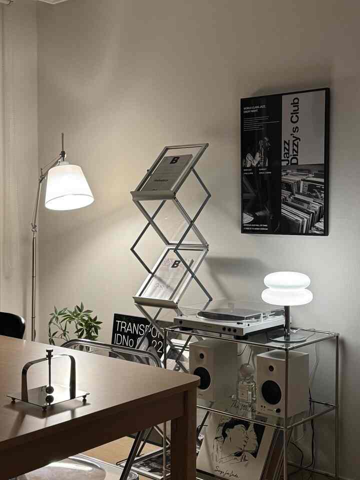 モノトーンの寝室、白いターンテーブルと照明が配置された棚があり、ミニマルな雰囲気のインテリア