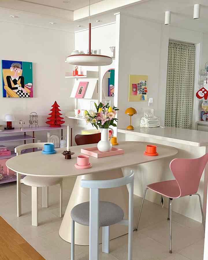 Beige and pink toned dining room featuring a diverse set of colorful dining chairs, table with flower vase and cups creating cozy atmosphere