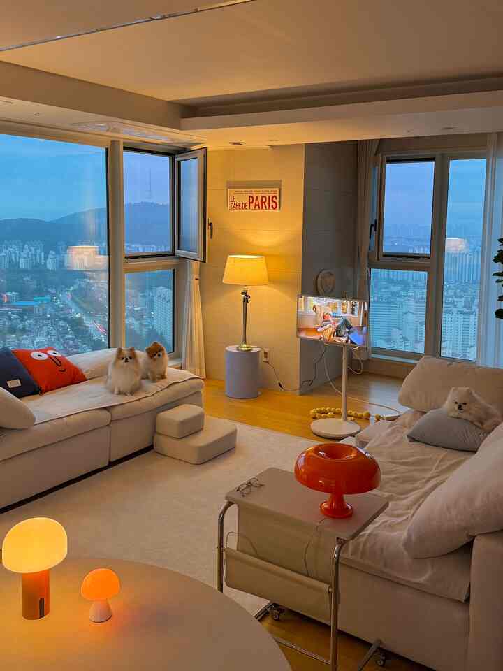 ホワイトとオレンジのトーンのリビング、広いソファとテーブルランプ、ペット3匹、広大な大きな窓を備えた居心地の良いモダンなインテリア