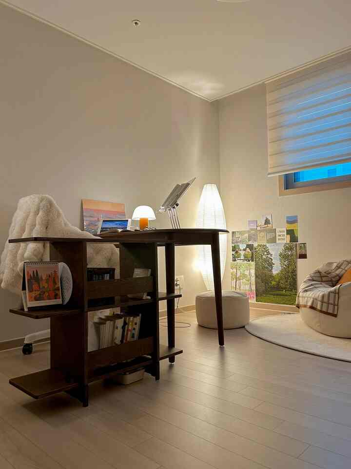 ベージュ色の壁と木目調の床が特徴のコンパクトなホームオフィス、木製の机とビーンバッグ、ランプが配置された雰囲気のある空間