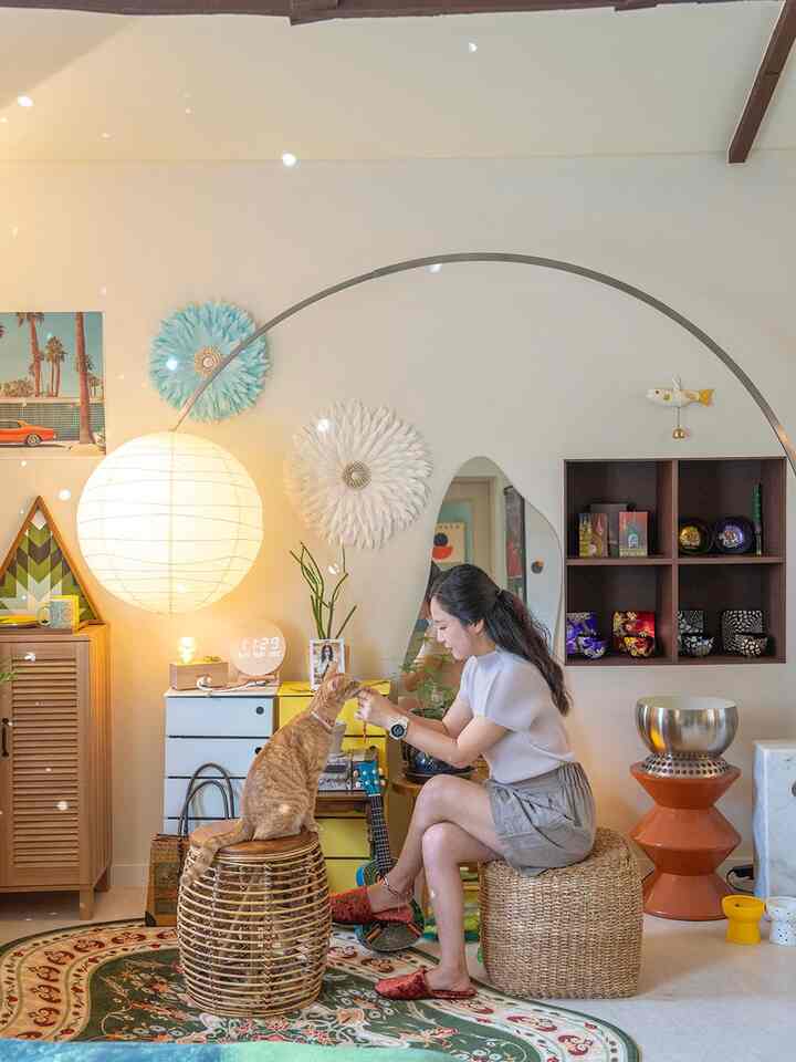 Natural-colored living room featuring rattan stools, an orange cat, unique mirror, and warm lighting creating a cozy atmosphere