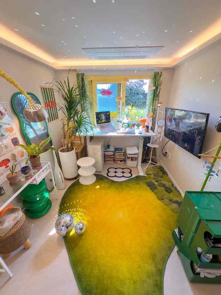 A small home office space in yellow and green tones featuring a desk with a laptop, plants, and a gradient rug creating a cozy work environment