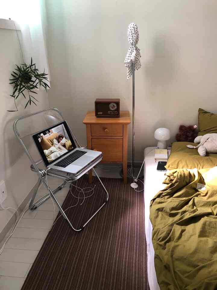 White-toned bedroom with wood tone furniture featuring a transparent folding chair and green hanging plant in a simple, tidy space