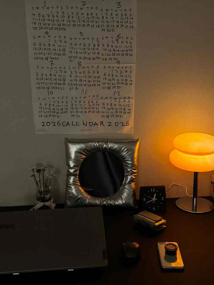 ブラックとシルバーのトーンのホームオフィス、デスク上にクッションミラーとテーブルランプが配置されたシンプルでモダンなワークスペース