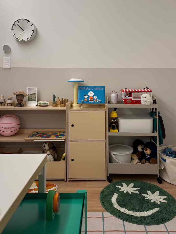 Natural tone kids' room with playful storage units, bookshelves filled with toys, and a round green carpet with a smiley face