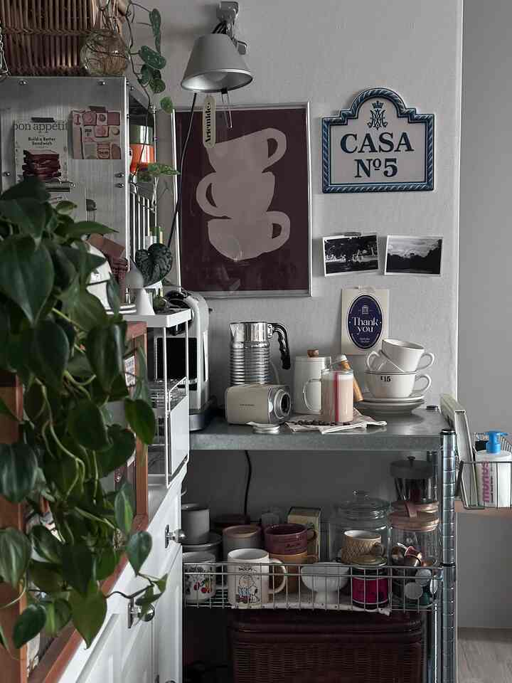 A compact home cafe space in gray and white tones, featuring metal shelves, coffee machines, and neatly arranged mugs