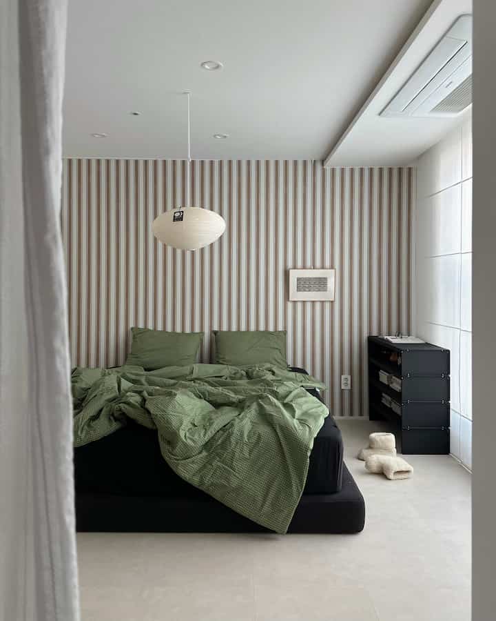 ベージュとブラウンのストライプ壁紙にディープグリーンのチェック柄寝具が配置された落ち着いた雰囲気のヴィンテージ寝室