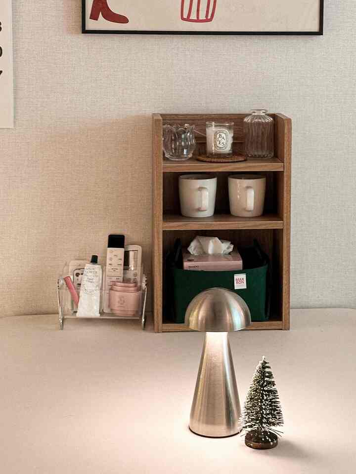 ウッドトーンの収納棚とシルバーのキノコ型テーブルランプが置かれた、シンプルで温かみのある小さなテーブルスペース