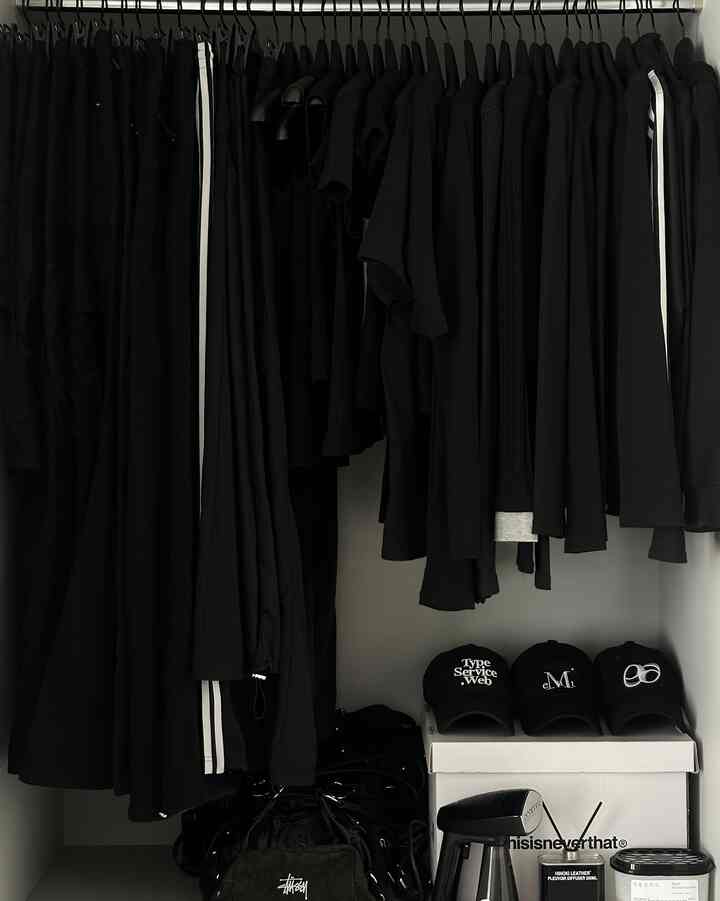 Closet space dominated by black clothes hanging neatly, with hats, boxes, and storage items organized below