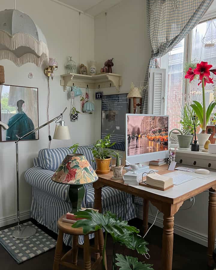 Natural-toned compact home office featuring wooden table, striped sofa, and various plants creating cozy atmosphere