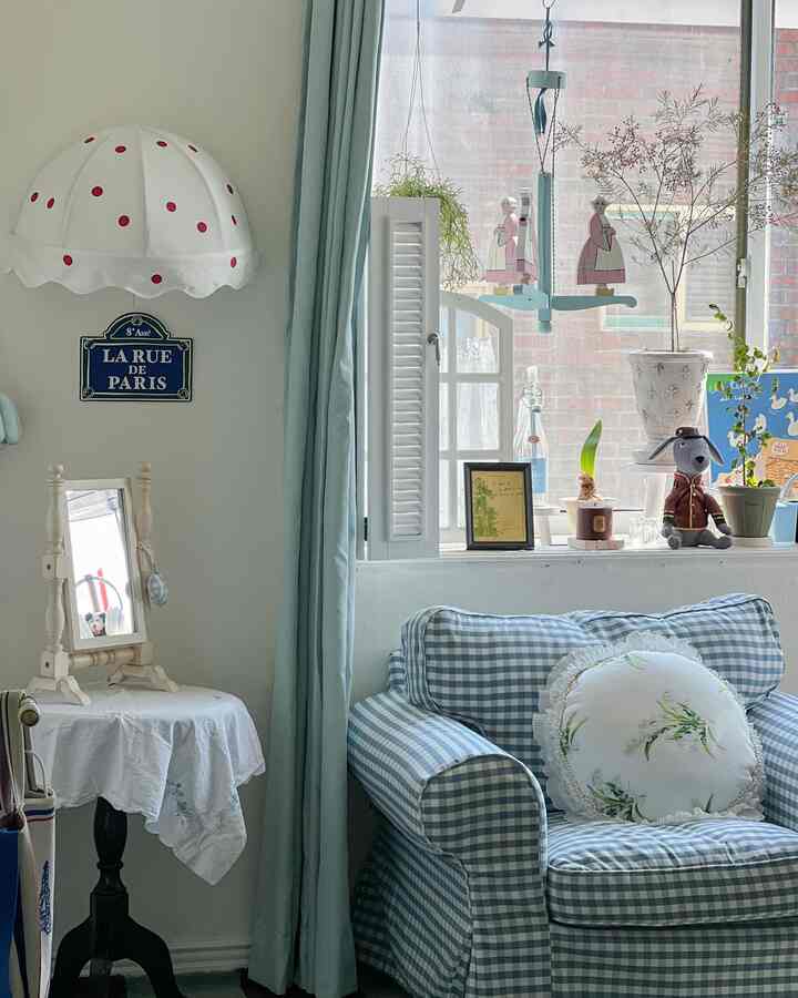 パステルブルーとホワイトのトーンのリビングルーム、ブルーチェックのソファとカーテン、植物、フレンチカントリーの装飾が配置された雰囲気のあるインテリア