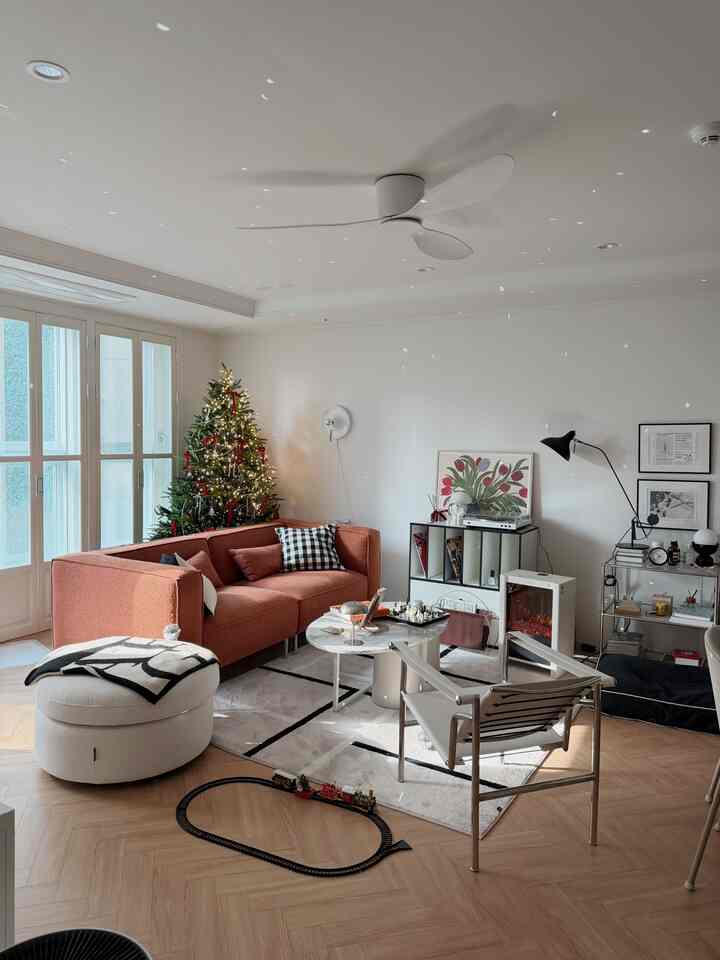 Natural modern living room with white walls and brown floor, featuring a red sofa and decorated Christmas tree, cozy atmosphere