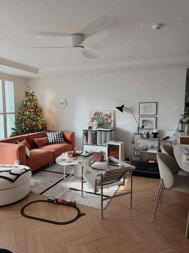 Bright living room with white walls and floor featuring a modern red sofa and decorated Christmas tree