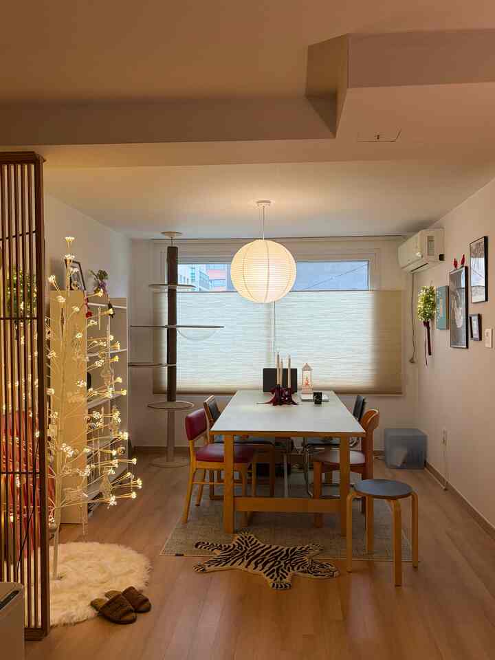暖かいベージュとブラウンの色調の4人用ダイニングルーム、キャットタワーと丸いペンダントライトが配置された自然な雰囲気の空間