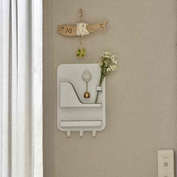 A warm beige wall entrance featuring a white magnetic storage unit with a fish-shaped charm and small flower decoration, evoking a natural and clean atmosphere