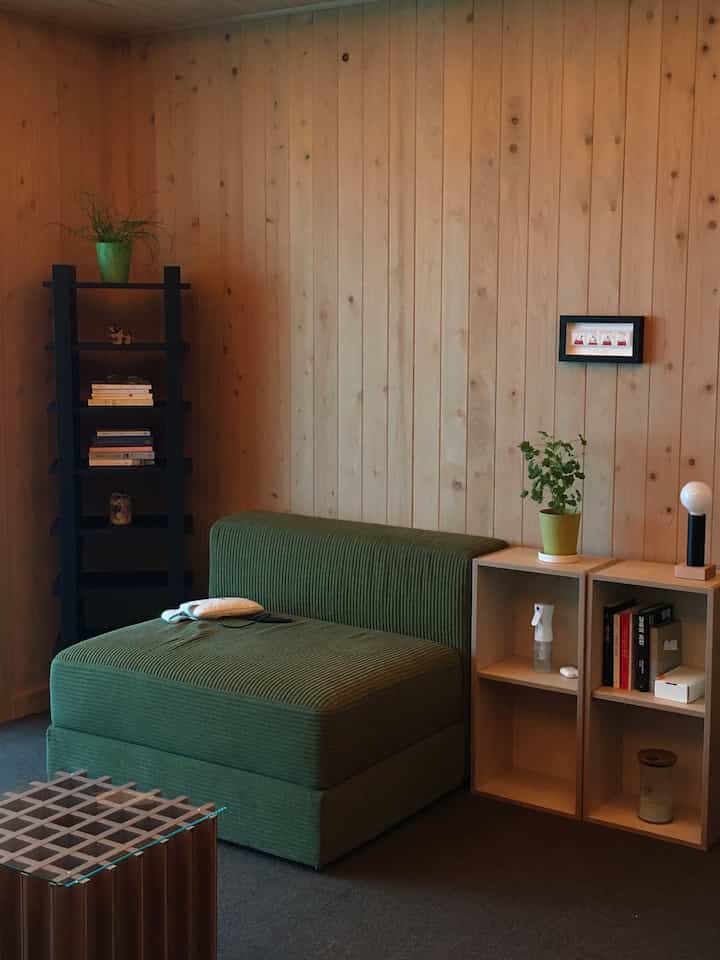 Living room with natural wood tone wall, green armchair, bookshelf, and sideboards creating a simple atmosphere
