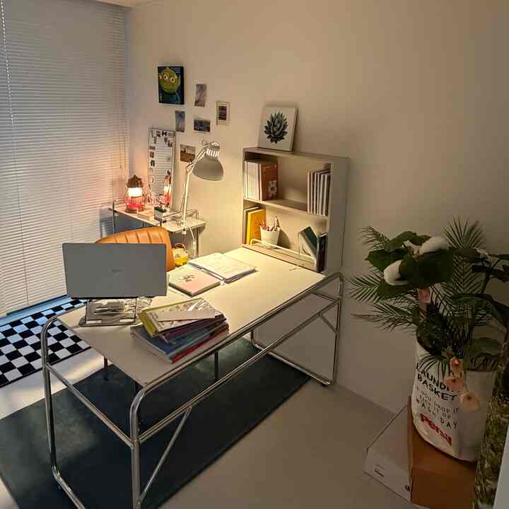 A compact white and black home office featuring a mid-century modern armchair, desk, plants, and cozy study ambiance