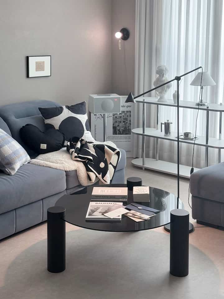 Modern living room in black and white tones featuring a central black coffee table, gray sofa with cushions, and sleek shelving