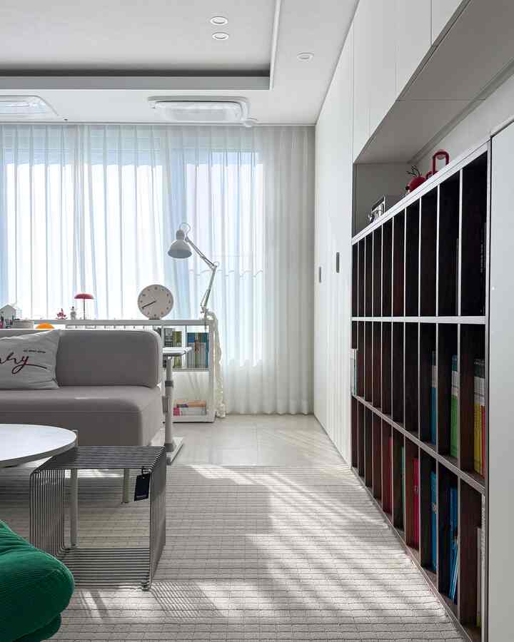 Bright living room in white and beige tones featuring a large bookshelf, sofa, and desk, creating a clean home office area