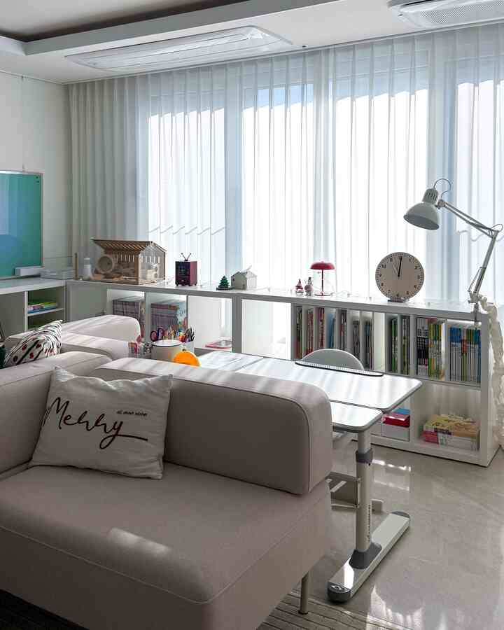 Bright white-toned living room and kids' space featuring beige sofa, white desk, and bookshelf in a simple modern style