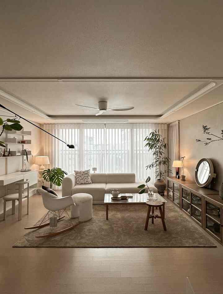 アイボリーとブラウンのトーンでまとめられたコージーなリビング、L字型ソファとアームチェア、植物、壁照明が配置された自然なインテリア