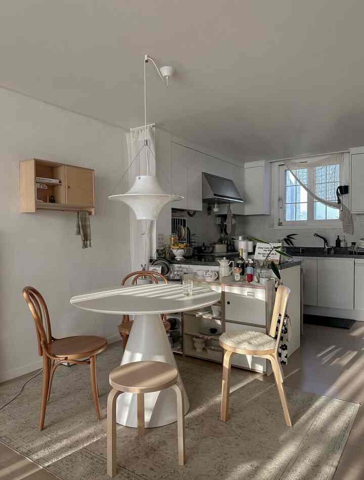 ナチュラルモダンな白いキッチンと丸いダイニングテーブル、木製のダイニングチェアが配置された雰囲気のあるダイニングルーム