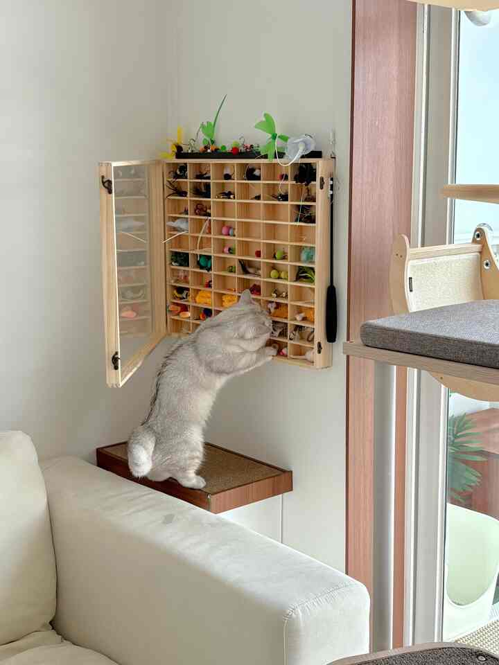 ベージュのソファがあるリビングの一角に壁掛けされた猫のおもちゃ収納がある、ナチュラルな雰囲気の猫と暮らす空間