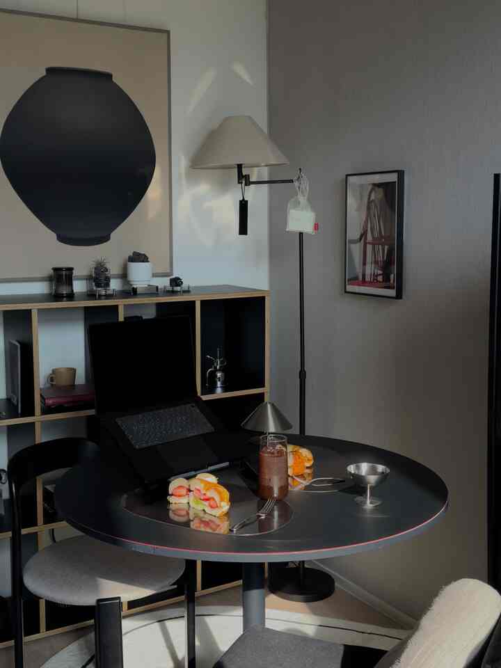 ブラックの色調のダイニングルーム、丸いダイニングテーブルと椅子、フロアランプ、ラグがあるモダンでシンプルな空間