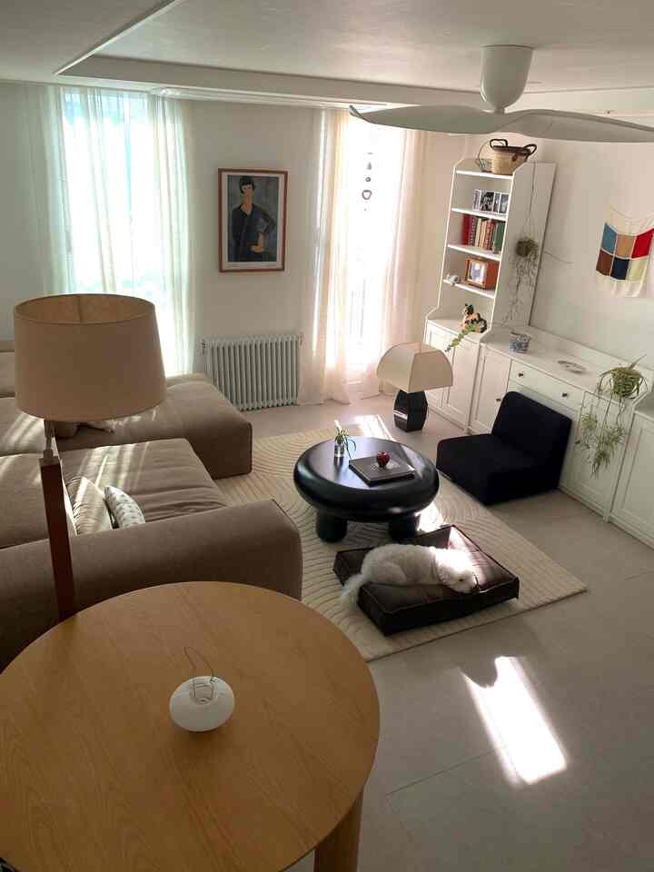 ベージュと白を基調としたリビング、広いソファと丸いコーヒーテーブル、ペットベッドに寝る犬が配置されたナチュラルな空間