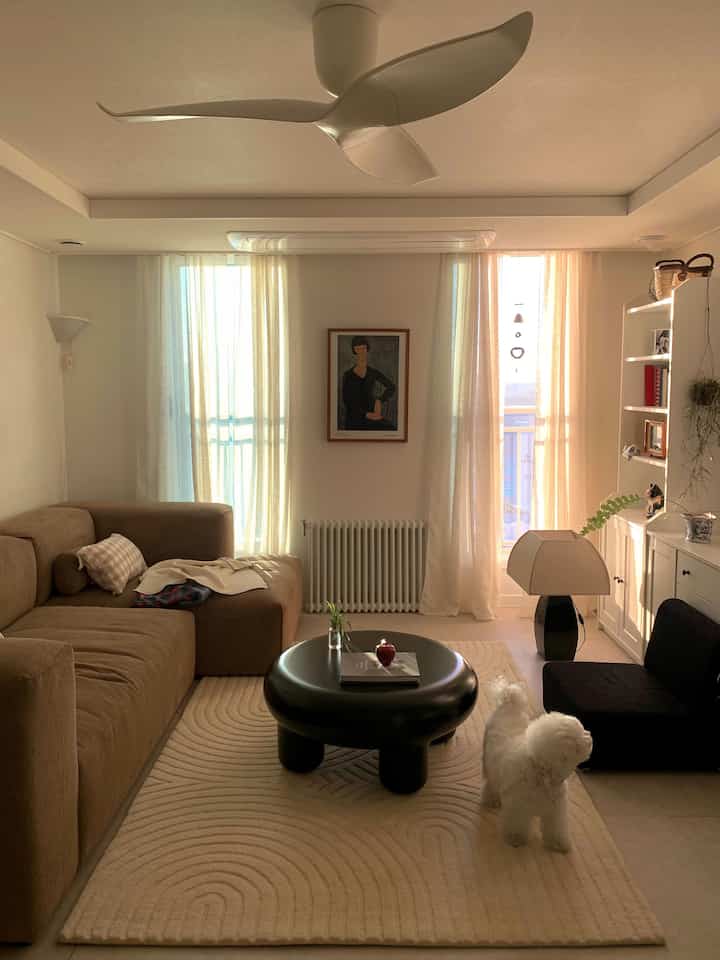 Bright living room in white and brown tones, featuring large brown sofa, sheer curtains, and central framed portrait creating cozy atmosphere