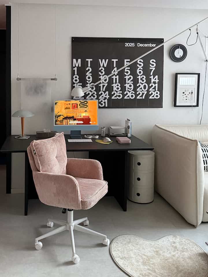 Modern and simple home office space featuring a pink office chair and black desk with a large calendar